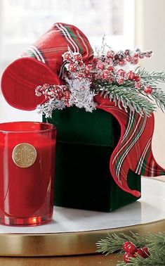 a red candle sitting on top of a table next to a green box with a bow