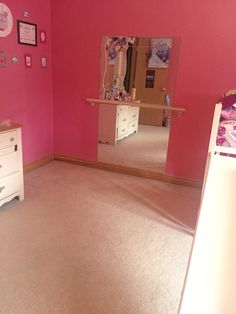 a bedroom with pink walls and white dressers in front of a mirror on the wall