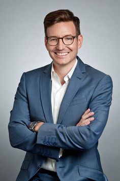 a man in a blue suit and glasses is posing for the camera with his arms crossed