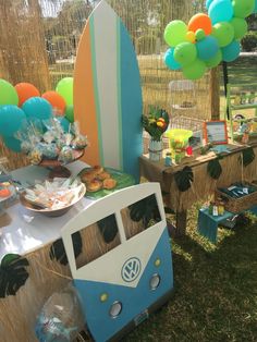 a vw camper van parked in front of a surfboard and dessert table