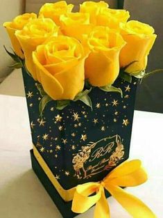 a bouquet of yellow roses sitting in a black box with gold stars on the side