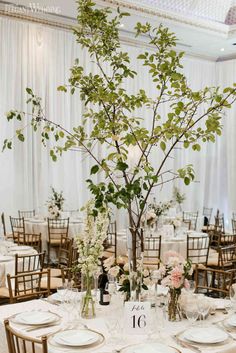 two tall vases filled with flowers and greenery on top of a white table