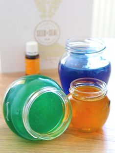 three jars filled with different colored liquid on top of a wooden table next to bottles