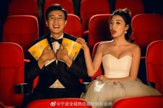 a man and woman sitting on red chairs in front of each other holding fan shaped fans