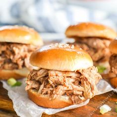 three pulled pork sandwiches sitting on top of a wooden cutting board