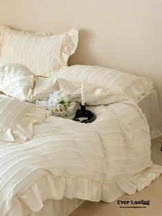 a bed with white comforter and pillows on it, next to a vase filled with flowers