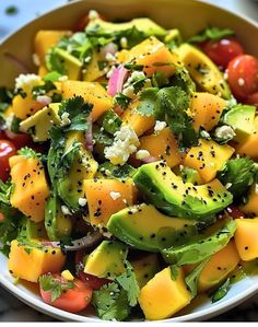 a salad with avocado, tomatoes, and other vegetables in a white bowl