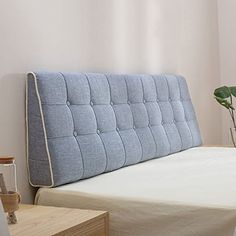 a bed with a blue upholstered headboard next to a plant in a vase