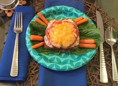 a blue plate topped with meat covered in cheese and carrots next to silverware