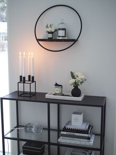 a shelf with candles and books on it in front of a mirror that is reflecting the wall