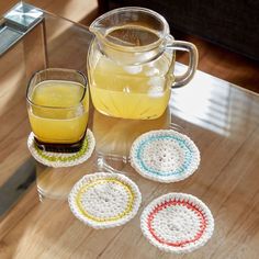 three crocheted coasters on a table next to a pitcher and glass cup