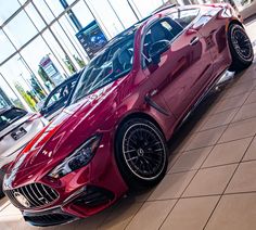 a red sports car parked in front of a glass building with other cars behind it