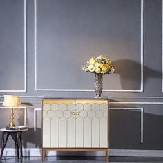 a vase filled with yellow flowers sitting on top of a cabinet next to two tables