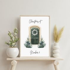 a christmas card with a green door and wreath on it next to a potted plant