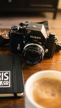 a camera sitting on top of a wooden table next to a book and cup of coffee