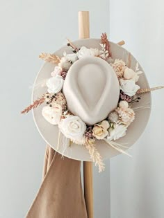 a white hat on top of a wooden stick with flowers and leaves around it, next to a tan napkin