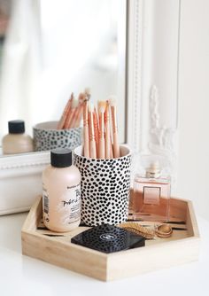 makeup brushes, lipstick and other items sit on a tray in front of a mirror