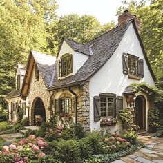 a white house with black shutters and stone walkway leading to the front door is surrounded by lush greenery