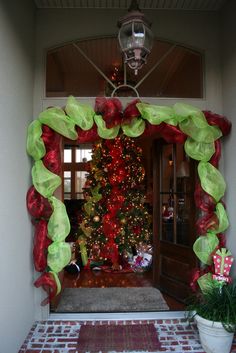 a decorated christmas tree sitting in front of a door with red and green ribbons on it