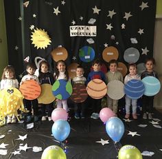 a group of children standing next to each other in front of balloons and paper cutouts