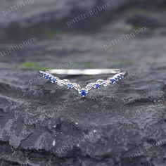 a silver ring with blue sapphire stones on top of a rocky surface in front of some grass