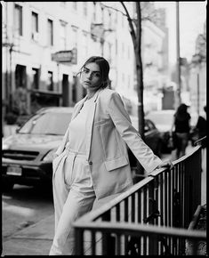 black and white photograph of woman in suit leaning on railing next to street with cars