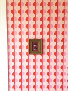 a pink and red wall with an eye looking at the viewer through a hole in the wall