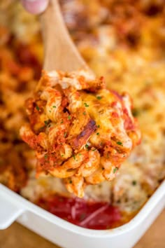 a wooden spoon is holding up a cheesy casserole