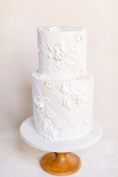 a three tiered white wedding cake with flowers on the top and bottom, sitting on a wooden stand