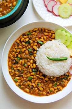 two bowls filled with beans and rice on top of a white table next to vegetables