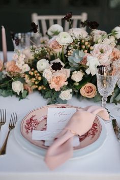 an elegant table setting with pink and white flowers on the centerpiece, silverware, and napkins