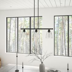 a dining room table with candles and vases on it next to large windows that look out onto the woods