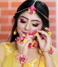 a woman with flowers in her hair and makeup looks at the camera while wearing a yellow outfit