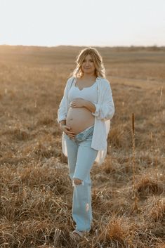 a pregnant woman standing in a field with her belly tucked under her shirt and jeans