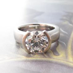 a diamond ring sitting on top of a white cloth covered table with an artistic background