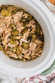 a white crock pot filled with shredded chicken and pickles next to some bread