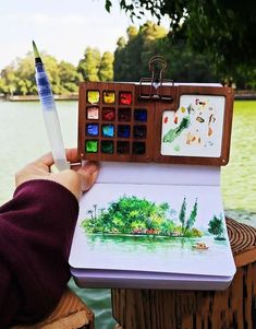 a person is holding a watercolor pencil and an artist's notebook with pictures on it