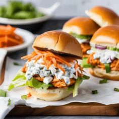 three chicken burgers with lettuce, carrots and ranch dressing on a cutting board