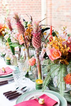 the table is set with pink and yellow flowers in vases, silverware, and plates