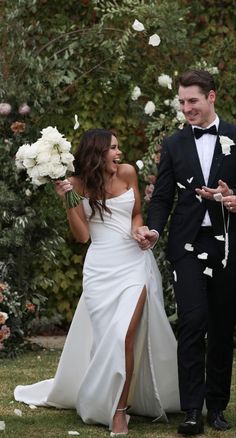 a bride and groom walking down the aisle with white flowers in their hand as confetti flies around them