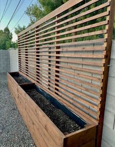 a wooden planter filled with gravel next to a fence