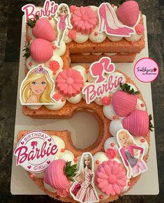 a cake shaped like the number 5 with barbie decorations on it and pink icing