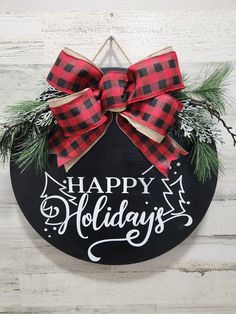 a happy holidays sign hanging on the side of a wooden wall with a bow and evergreen