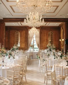 a room filled with lots of tables covered in white clothed tablecloths and tall chandeliers