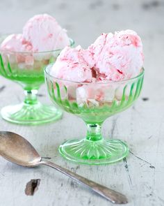 two green glass bowls filled with ice cream on top of a white wooden table next to a spoon