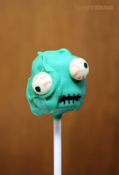 there is a green cake on a stick with eyes and mouthballs painted on it