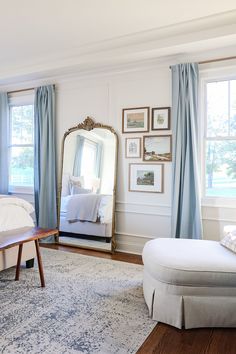 a bedroom with a large mirror and blue drapes on the windowsill, along with a white bed