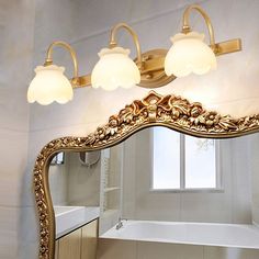 a bathroom mirror with three lights and a bathtub in front of the mirror on the wall