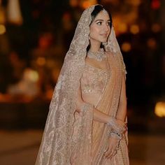 a woman in a bridal gown and veil standing on the street at night with city lights behind her