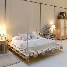 a white bed sitting inside of a bedroom on top of a wooden pallet next to two lamps